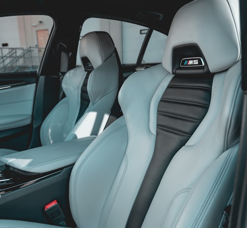 The interior of a car featuring luxury sports seats with a sleek design. The seats are predominantly light grey with black accents and have noticeable logos on the headrests. There is a spacious middle console and visible car doors showcasing a modern and upscale finish.
