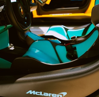 The interior of a luxury sports car is featured, showcasing sleek black and turquoise seats, a stylish steering wheel, and prominent branding on the dashboard. The car's door is open, revealing an elegant design with a vibrant orange exterior.